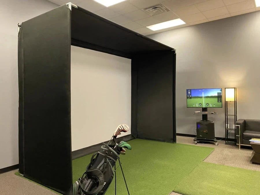 The AllSportSystems Super Bay™ LITE™ Golf Simulator Safety Bay features a screen, projector, and an elegant set of clubs on a green mat. A television display showcases the immersive simulation interface, ideal for improving your golfing skills.