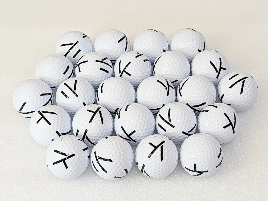 A set of GolfJoy GDS Plus Launch Monitor balls, with black X markings on a white surface, is ready to shine in your favorite golf simulator programs.