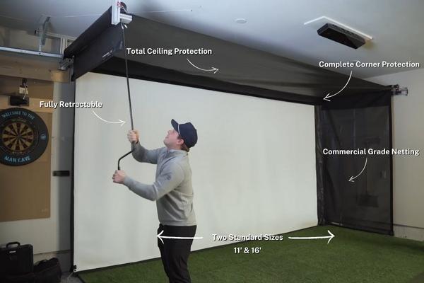 A person demonstrates the SportScreen Vanish by AllSportSystems, showcasing features like total ceiling and complete corner protection, commercial grade netting, and two standard sizes (11' & 16'), with a dartboard on the wall.