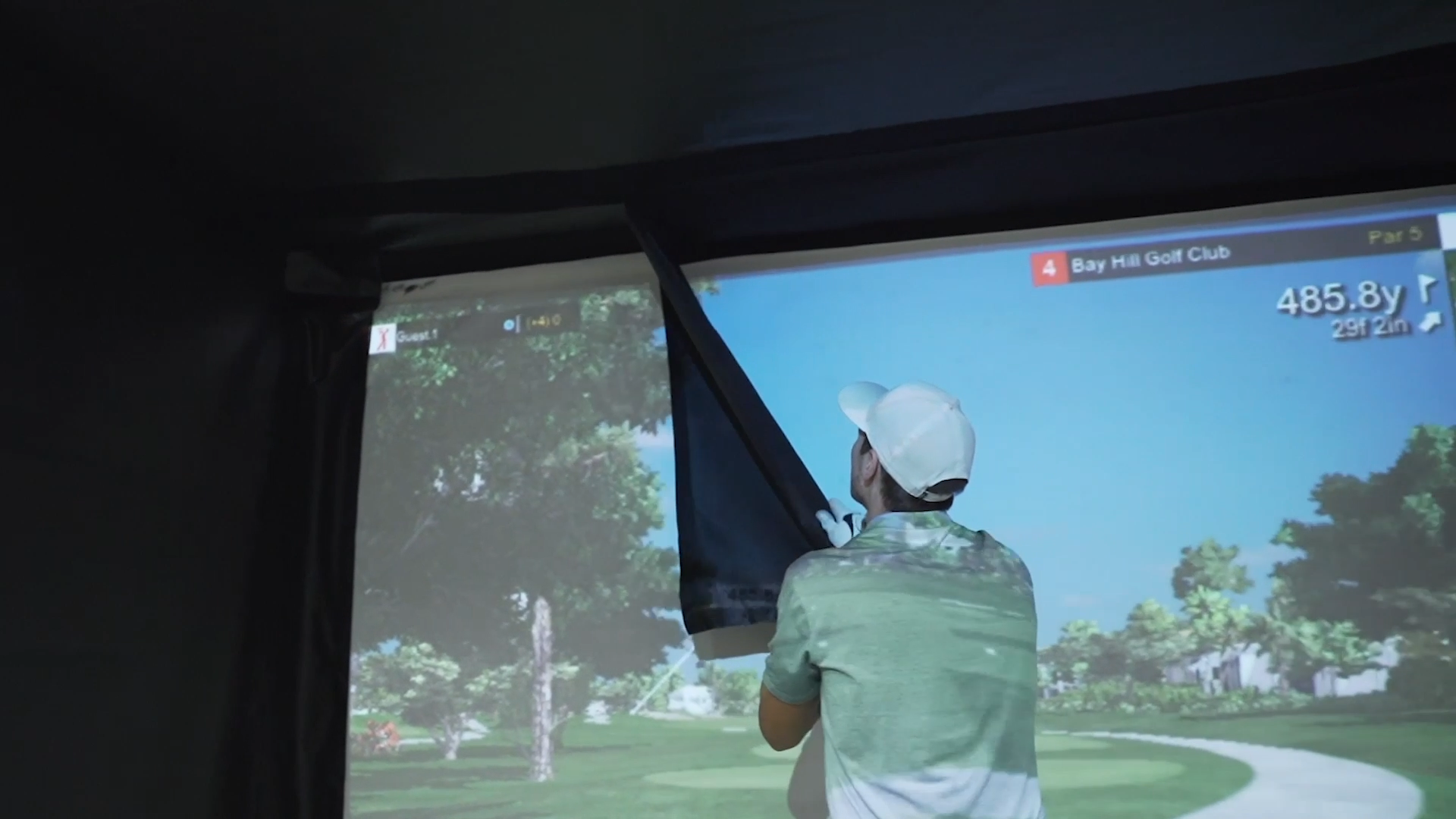 A person using the AllSportSystems SportScreen Vanish Retractable Golf Bay views a virtual golf course on a large screen in a simulator room.