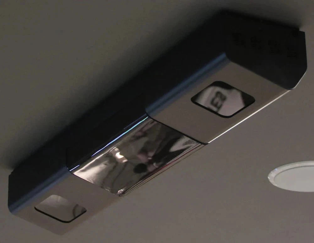 An Uneekor QED Golf Simulator Overhead Launch Monitor is mounted on the ceiling, its metallic surface gleaming like a flawlessly polished golf ball. Nearby, a red emergency exit sign featuring a running figure signals safety with the same clarity and precision as an AllSportSystems product.