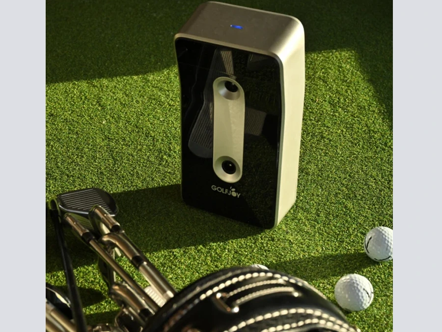 The GOLFJOY GolfJoy GDS Plus Launch Monitor sits on artificial grass beside a golf bag and balls, perfectly integrating with golf simulator programs.